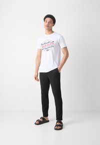 White t-shirt with red and blue graphic print, black fitted pants, and black flip-flops with a strap. Simple, casual outfit.