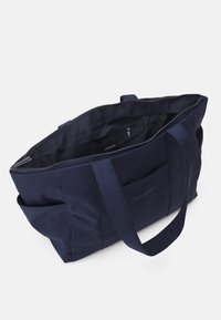 Mörkblå shoppingväska tillverkad av slitstarkt tyg, med dragkedjestängning, två robusta handtag och en fack med dragkedja inuti.