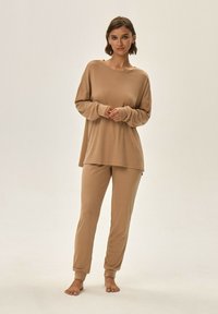 Beżowy zestaw loungewear składający się z luźnej, długiej bluzki z długim rękawem oraz taperowanych spodni, wykonany z miękkiego materiału o gładkiej teksturze.