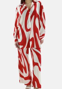 Ensemble de pyjama rouge et blanc à motifs, comprenant une chemise à manches longues avec boutons et un pantalon à jambes larges, confectionné dans un tissu lisse.