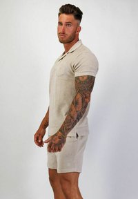 Beige kortärmad polo med matchande shorts i texturerad tyg. Har en bröstficka och sidofickor för ökad komfort.
