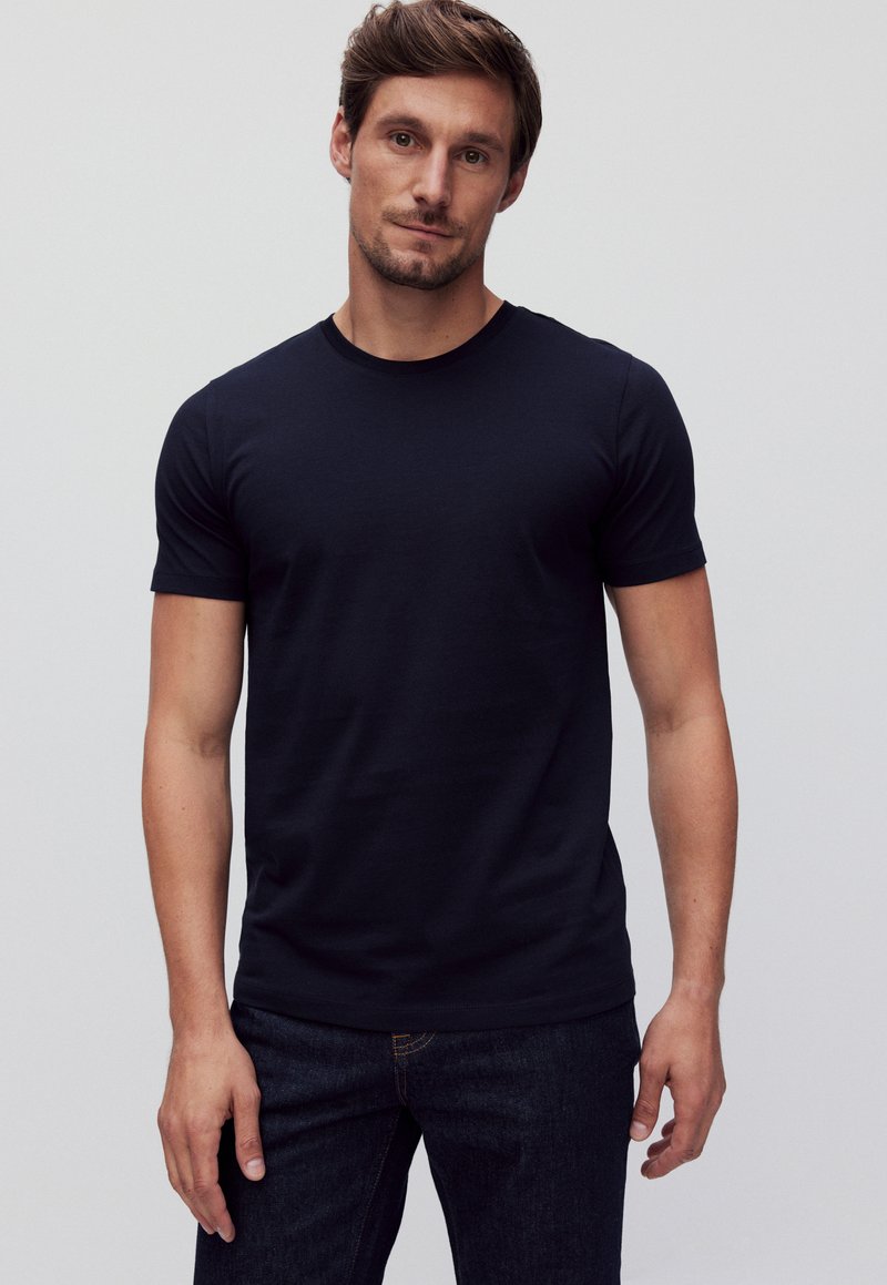 Heren navy blauwe t-shirt met korte mouwen van katoen, voorzien van een ronde hals en een slim fit, gecombineerd met donkere denim jeans.