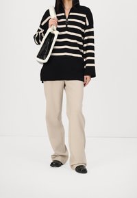 Jersey de rayas negras y beige con cuello de media cremallera, combinado con pantalones beige de pierna ancha y zapatos negros sin cordones. También se destaca un bolso texturizado.