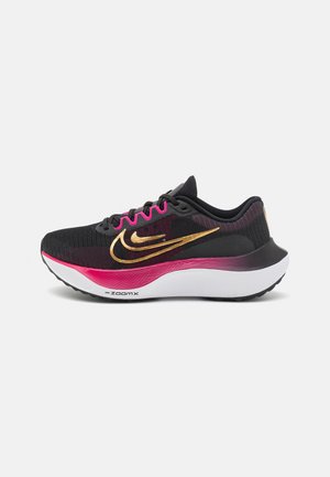 Schwarzer Laufschuh mit pinken Akzenten, goldenem Nike-Swoosh, weißer ZoomX-Sohle und schwarzen Schnürsenkeln vor einfachem hellem Hintergrund.