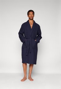 Navy blue waffle-textured bathrobe with long sleeves, a belt tie, and two front pockets. Knee-length design.