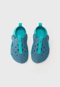 Mörkblå och teal slip-on skor med en texturerad gummiöverdel, flera ventilationshål och en dragrem för enkel påtagning.
