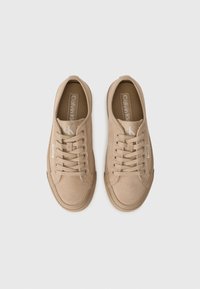 Beige suede sneakers with round toe, lace closure, and padded collar. Features logo accents on the tongue and side. Flat rubber sole.