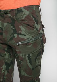 Spodnie cargo z kamuflażem w ciemnozielono-brązowej kolorystyce, wyposażone w kieszeń na zamek oraz trwały materiał zapewniający funkcjonalność.
