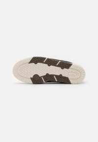 Texturált barna gumi tapadású talpú sneaker, fehér körös mintákkal és zöld akcentusokkal. Masszív, ívelt kialakítással a tartósság érdekében.