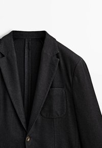 Blazer grigio scuro a un bottone con rever a toppa e tasca frontale, esposto su uno sfondo bianco.