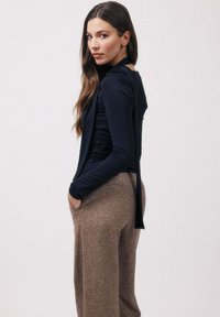 Haut bleu marine à manches longues avec un design drapé et des liens dans le dos, associé à un pantalon taille haute texturé de couleur brun clair avec des poches.