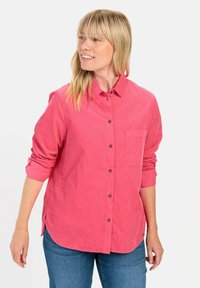 Roze button-up shirt met een borstzak, opgerolde mouwen en een gebogen zoom. Gemaakt van een gestructureerde stof met donkere knopen.