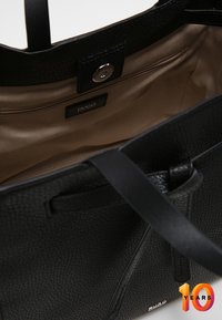 Sort læder tote taske med tekstureret ydre, en glat beige indvendig, en lynlåslomme og et mærkeskilt synligt indeni.