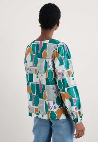 Blusa a maniche lunghe con motivo, caratterizzata da forme geometriche verdi, viola e arancioni su uno sfondo bianco; tessuto leggero, vestibilità morbida.