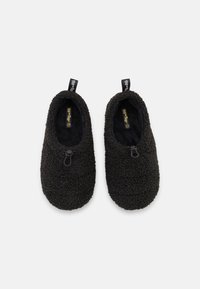 Black fleece slippers with a soft texture, rounded shape, and no visible fastenings. Includes branding tags on the back.