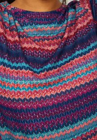 Top multicolore con un motivo a zigzag nei toni di blu, rosso, arancione e viola. La trama del tessuto appare liscia e lavorata a maglia.