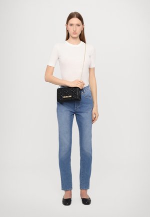 Borsa nera trapuntata con dettaglio del logo dorato, abbinata a una camicia bianca aderente e jeans blu a vita alta. Le semplici ballerine nere completano l'outfit.