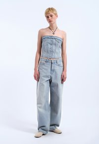 Ljusblå denimstrapless topp med knäppning i fronten, som matchas med löst sittande ljusblå jeans och beiga slip-on skor.