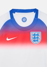 Hvit sportsdrakt med en gradient fra rød til blå på toppen, med Nike-logoen og Englands emblem på forsiden. Teksturert stoff.
