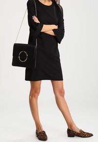 Musta ribbed-mekko, jossa on kellohelmat, yhdistettynä jämäkkään mustaan käsilaukkuun, jossa on pyöreä metallikoriste ja eläinkuosiset loaferit.