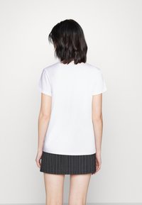 Bílý krátký rukáv tričko s kulatým výstřihem v kombinaci s pruhovanou černou mini sukni. Tkanina vypadá hladce a lehce.