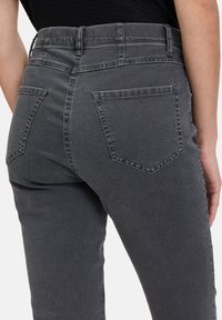 Des jeans en denim gris présentent une coupe ajustée avec une taille haute, des poches arrière et des détails de couture visibles le long des coutures.