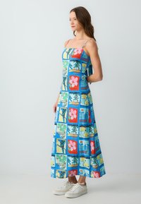 Maxikleid aus blauem Stoff mit einer Collage aus bunten Blumen- und tropischen Mustern, mit dünnen Trägern und einer lockeren Passform.