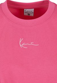 Roosa puuvillane T-särk ümmarguse kaelusega ja valge kätkiv logo. Kangas on pehme tekstuuriga ja sile viimistlus. Suurus M.