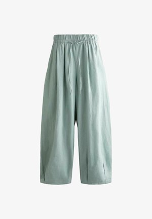 Pantalon ample vert clair à jambes larges avec taille élastique et cordon à l'avant, présentant de petites fentes à l'ourlet.
