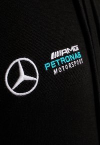 Tessuto nero con logo Mercedes-Benz ricamato in bianco e testo "AMG Petronas Motorsport" in bianco e turchese.