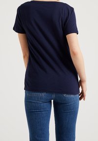 Camiseta azul marino de manga corta con cuello redondo, fabricada en algodón suave. Presenta un ajuste relajado y un dobladillo recto a la altura de la cintura.