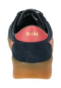 Zapatilla de ante azul marino con detalles en cuero rojo, que cuenta con un talón acolchado y una suela de goma. Marca dorada en el talón.