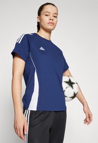 Navy sports t-shirt with white side panels, featuring a small logo on the chest and three stripes on the sleeves. Player holding a soccer ball.