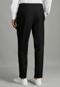 Pantalons noirs avec une taille élastique. Texture lisse, design ajusté, chevilles resserrées et deux poches arrière. Associés à des baskets blanches.