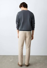 Grauer Pullover mit Rundhalsausschnitt, kombiniert mit beigen Slim-Fit-Hosen. Der Stoff wirkt weich, mit minimalistischem Design und ohne sichtbare Muster.