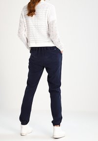 Bílý háčkovaný svetr s texturovaným vzorem a žebrovaným lemem, spárovaný s námořnickými zúženými tepláky s elastickým pasem a bočními kapsami.