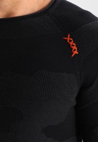 Czarny dzianinowy top z długim rękawem, ozdobiony teksturowanymi wzorami, pomarańczowym akcentem szwu na ramieniu oraz dopasowanym krojem.