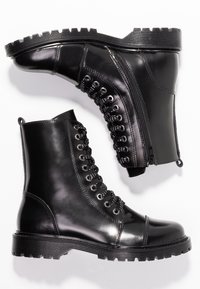 Un par de botas de combate de cuero negro con suelas gruesas, cordones delanteros y cremalleras laterales sobre un fondo blanco.