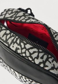 Pequeno saco com fecho de correr com padrão abstrato preto e branco, acabamento em couro preto e forro interior de tecido vermelho.