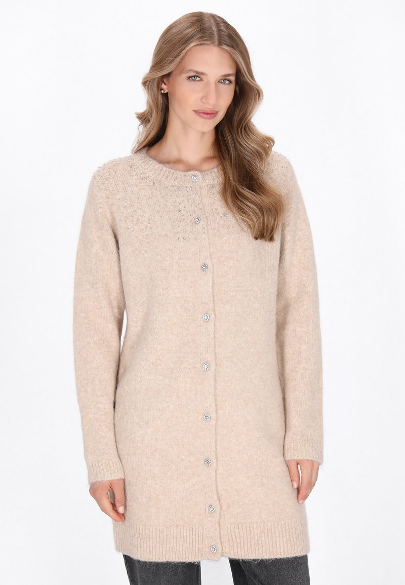 Beige gestrickte Strickjacke mit rundem Ausschnitt, langen Ärmeln und dekorativen Knöpfen. Weiche Textur mit geripptem Saum.