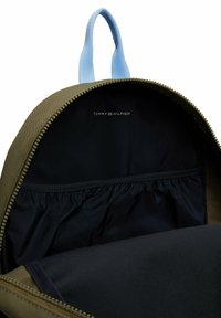 Zaino in tessuto verde con manico blu, dotato di un interno nero e tasca elastica. Logo del marchio visibile nella fodera interna.