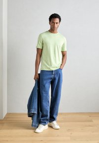 Un tricou scurt cu mânecă scurtă de un verde deschis, blugi ușori de culoare albastră, iar pe picioare adidași albi. Ține în mână o jachetă din denim închis. Design simplu, croială casual.