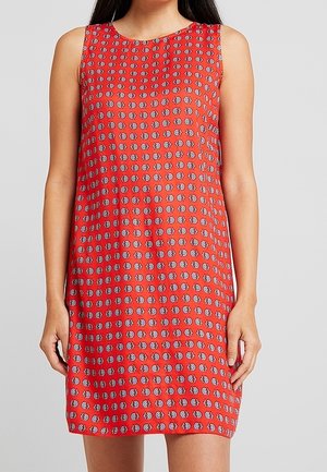 Robe rouge sans manches avec un petit motif floral circulaire blanc et noir répétitif, portée par une femme sur un fond uni.
