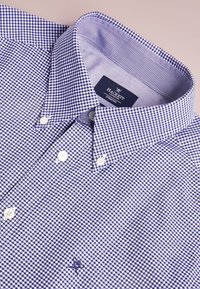 Chemise à carreaux bleu et blanc avec col à pointes, boutons blancs et logo brodé sur le côté gauche. Matière en coton.