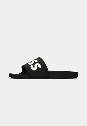 Sorte slidesandal med bred stropp som har hvit tekst. Laget av mykt materiale, designet med flat såle for uformell bruk.