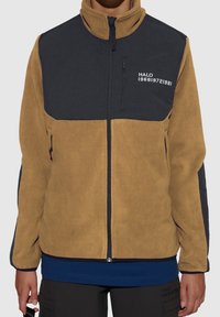 Tan fleece jacket with black upper section, zip closure, side pockets, and logo detailing. Features a stand-up collar and textured fabric.