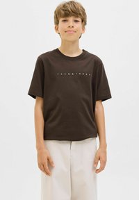 Ruda medvilnė marškinėliai su apvalia iškirpte ir trumpomis rankovėmis, priekyje su užrašu "JACK & JONES" baltos spalvos. Pora su smėlio spalvos kelnėmis.