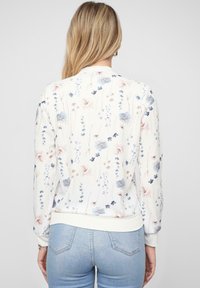 Sweatshirt à motif floral en crème clair avec des fleurs bleues et roses. Poignets et ourlet côtelés. Tissu doux avec une coupe décontractée.