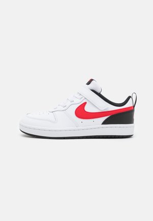 Baskets basses blanches avec le logo Nike rouge, talon noir, doublure intérieure noire, semelle blanche, lacets et une bride en velcro sur un fond uni.