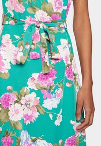 Vestido floral em tecido azul-escuro com flores rosas e brancas. Inclui um laço correspondente na cintura e uma textura suave.